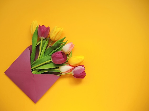 Tulipes multicolores dans une enveloppe violette pour la journée de la femme ou Pâques sur fond jaune