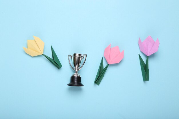 Tulipes en origami et coupe du vainqueur sur fond bleu Concept de victoire Mise à plat Vue de dessus