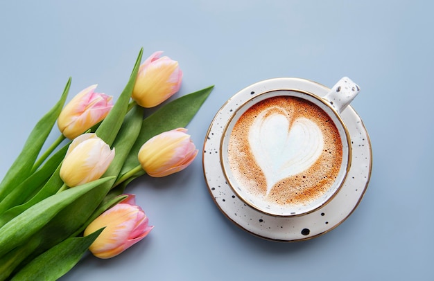 Tulipes de printemps et tasse de café sur un bureau bleu