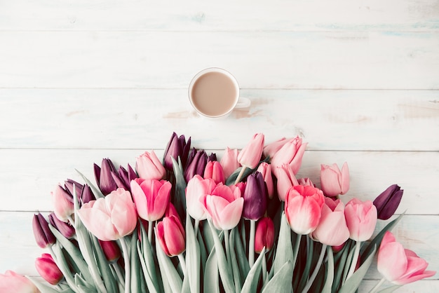 Tulipes de printemps et une tasse de café sur une table en bois blanc