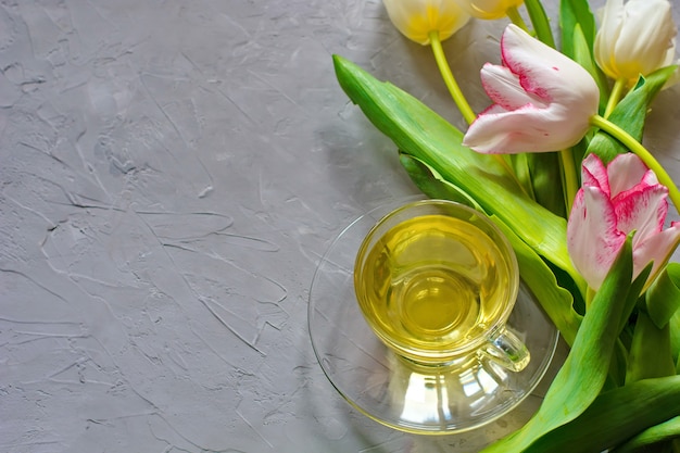 Tulipes de printemps tendres et une tasse de thé vert sur fond de ciment gris