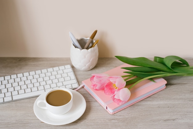 Tulipes roses avec une ambiance printanière festive et café sur une table en bois Travail des femmes, bureau à domicile et concept de carrière. Vue de côté