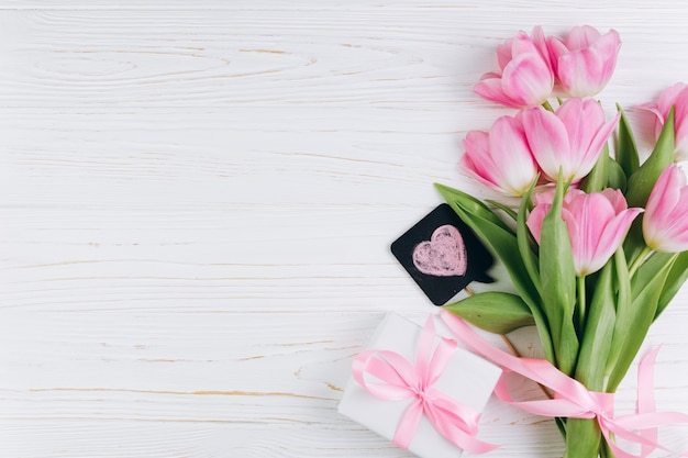 Tulipes roses et cadeau sur un fond en bois blanc