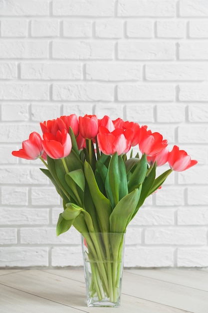 Tulipes roses dans un vase en verre sur fond de mur de briques blanches