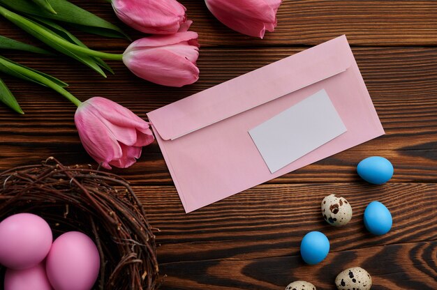 Tulipes Roses, Oeufs De Pâques Et Enveloppe De Voeux Sur Table En Bois. Fleurs De Printemps En Fleurs Et Nourriture Pascale, Décoration Florale Fraîche, Symbole De Célébration De Vacances