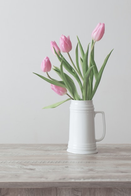 Tulipes roses en pot en céramique blanche sur table en bois sur fond blanc mur