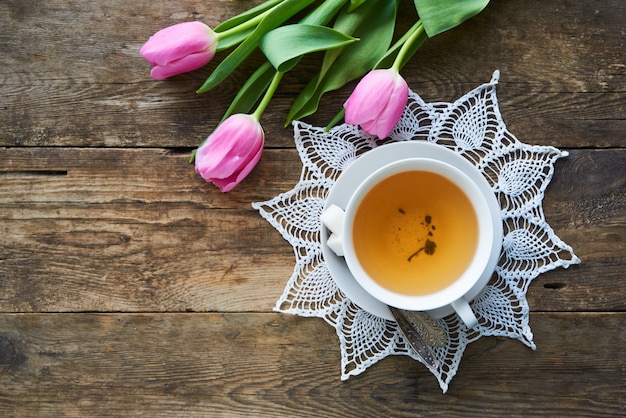 Tulipes roses et une tasse de thé vert sur une table en bois