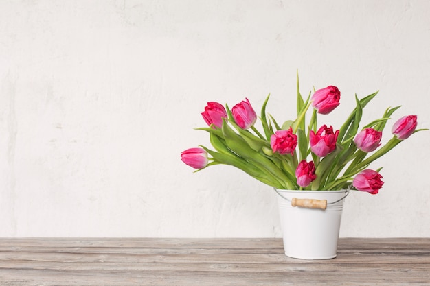 Tulipes rouges dans un seau sur fond vieux mur blanc