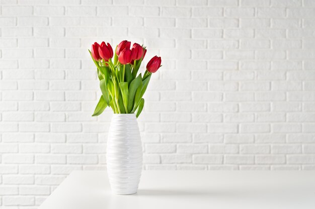 Tulipes rouges dans un vase blanc sur fond de briques blanches