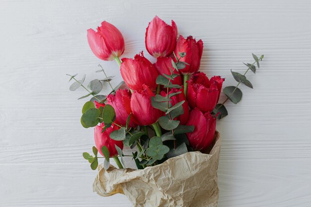 Tulipes rouges élégantes et bouquet d'eucalyptus en papier kraft sur la vue de dessus en bois blanc rustique