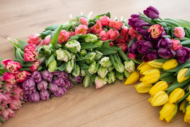 Des tulipes variées de couleurs roses, violettes, vertes et jaunes disposées sur un sol en bois