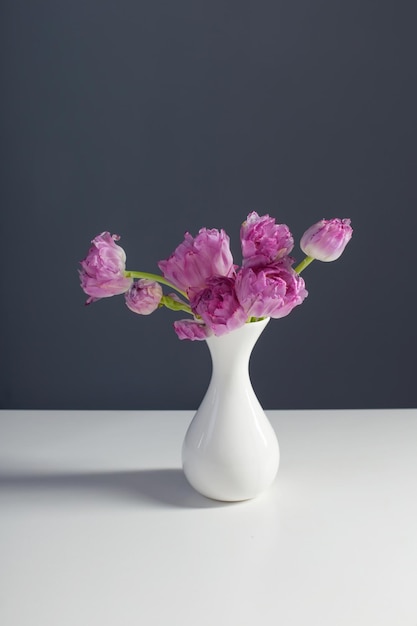 tulipes violettes dans un vase blanc sur fond de mur gris