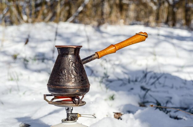 Turc en cuivre avec un manche en bois pour faire du café sur fond de neige dans les bois