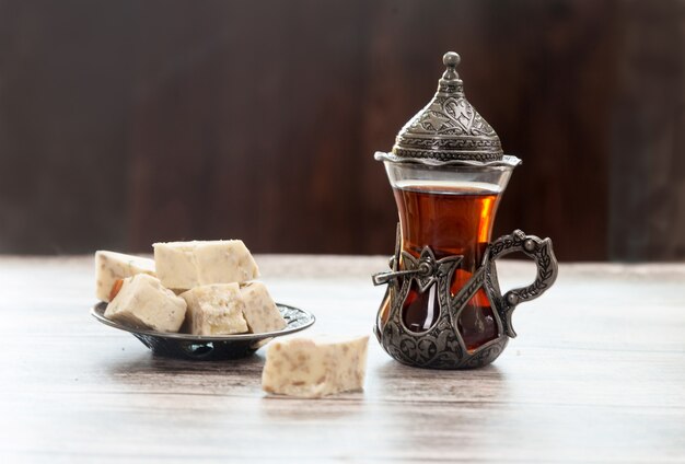 Turetius un verre de thé, une cuillère en métal et un halva de tournesol aux amandes et aux pistaches se dressent sur un fond en bois.