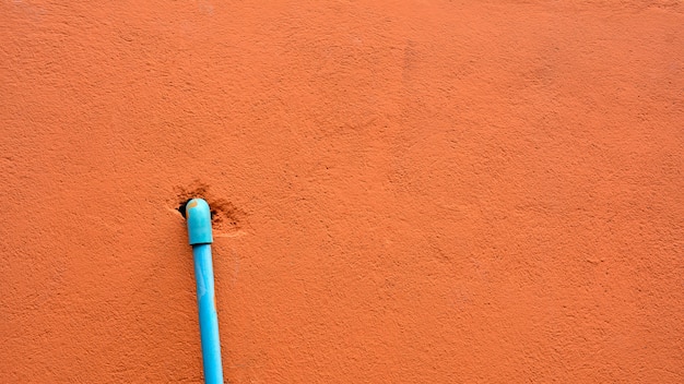 Tuyau en plastique bleu au mur de ciment orange.