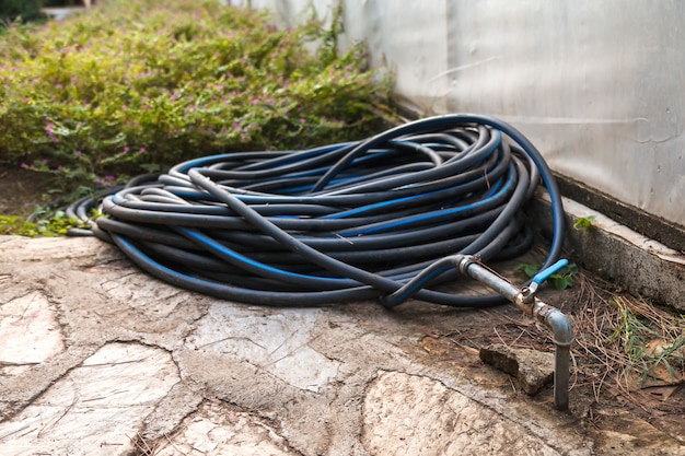 Un tuyau en plastique noir avec une bande bleue est tordu en anneaux et raccordé à un tuyau d&#39;eau dans la cour