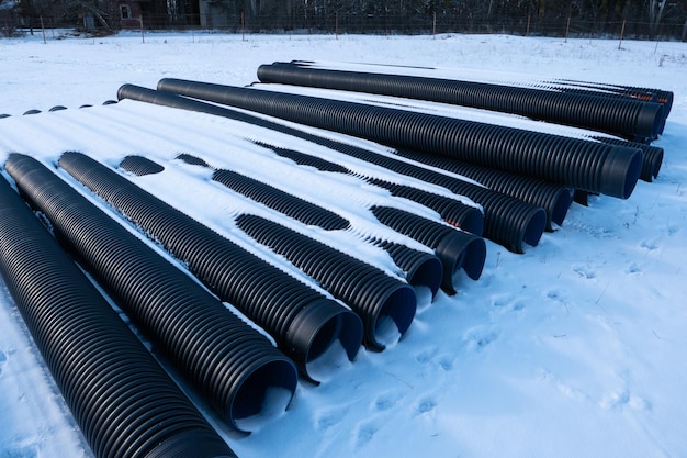 Des tuyaux de drainage en plastique ondulé noir disposés sur un champ enneigé