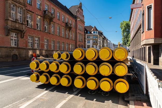 Des tuyaux isolés noirs avec des bouchons en plastique jaune empilés dans une rue de la ville Vieux bâtiments et ciel bleu