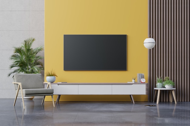 TV sur meuble dans un salon moderne avec fauteuil, lampe, table, fleur et plante sur mur jaune