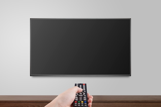 TV sur mur blanc avec la main à l'aide de la télécommande