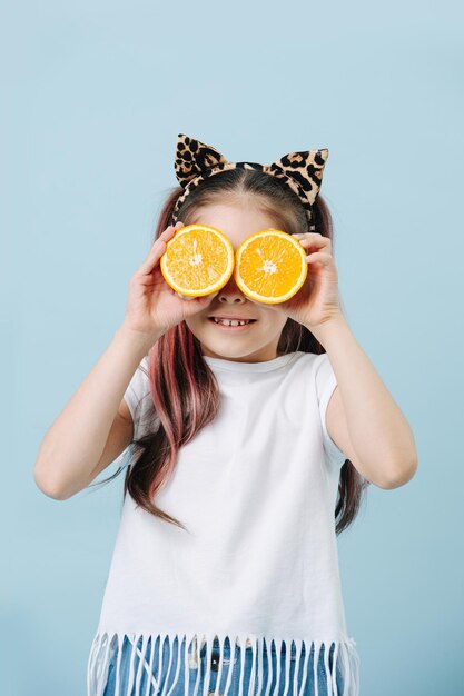 Tween girl drôle avec des oreilles de chat tenant des moitiés d'orange sur ses yeux