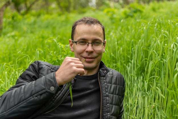 Un type assis sur de l'herbe avec un brin d'herbe dans les dents.