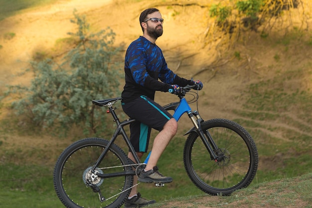 Type barbu brutal de sports sur un cycliste moderne de vélo de montagne sur les collines vertes au printemps