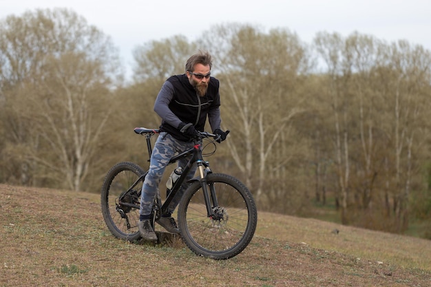 Type barbu brutal de sports sur un cycliste moderne de vélo de montagne sur les collines vertes au printemps