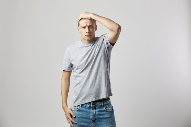 Un type blond sérieux vêtu d'un t-shirt blanc et d'un jean tient sa main sur la tête