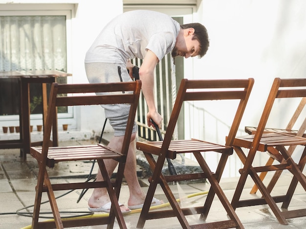 Un type caucasien lave des chaises de jardin en bois penchées avec Karcher