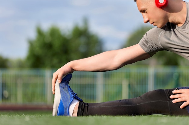 Un type caucasien pétrit ses jambes avant de faire du jogging dans le stade