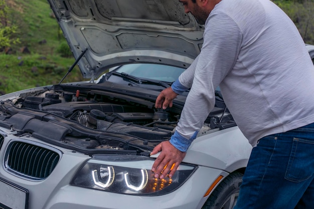 Le type ouvre le capot de la voiture et regarde le moteur.