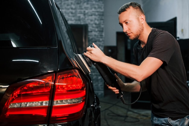 Type de polissage de la surface du véhicule L'automobile noire moderne est nettoyée par l'homme à l'intérieur de la station de lavage de voiture