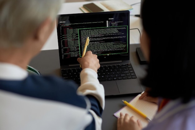 Un type avec un stylo pointant sur des codes sur l'écran d'un ordinateur portable lors de la présentation d'un nouveau logiciel à une camarade de classe et de l'explication du sujet de la leçon