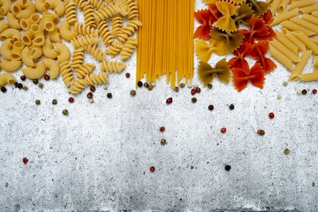 Types de pâtes alimentaires non cuites. Pâtes penne, fusilli, farfalle, spaghetti, chifferi et pois colorés sèchent sur un fond de béton léger. Lay plat, vue de dessus, espace de copie