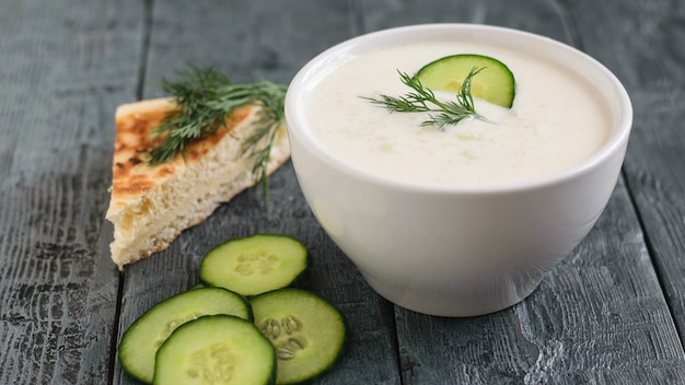 Tzatziki fraîchement préparé dans un bol blanc avec du concombre et du pain sur une table en bois foncé