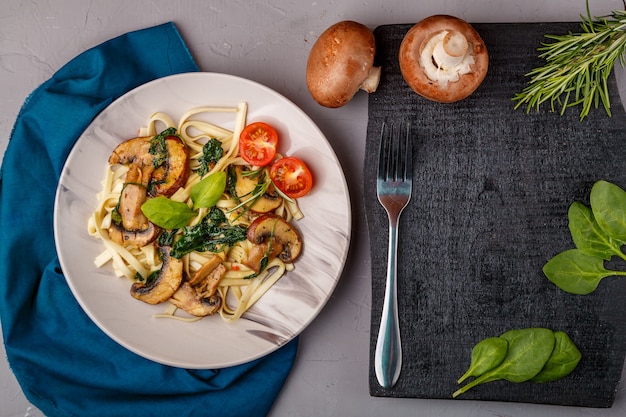 Udon aux champignons et épinards dans une assiette sur une serviette bleue sur une surface en béton près des champignons et des couverts sur le plateau