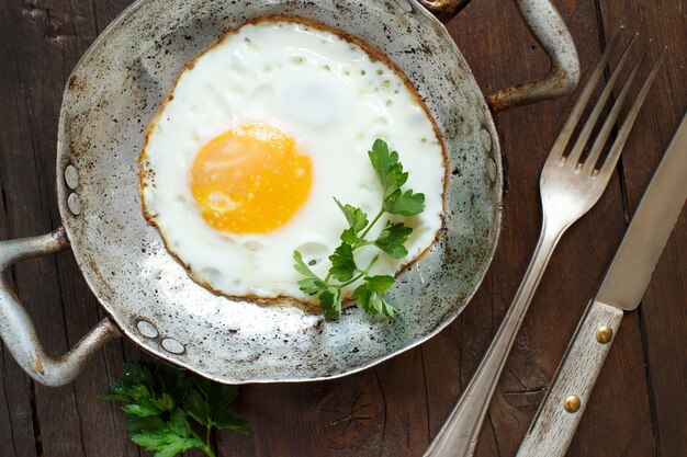 Œuf frit aux tomates et herbes dans une vieille poêle à frire sur bois