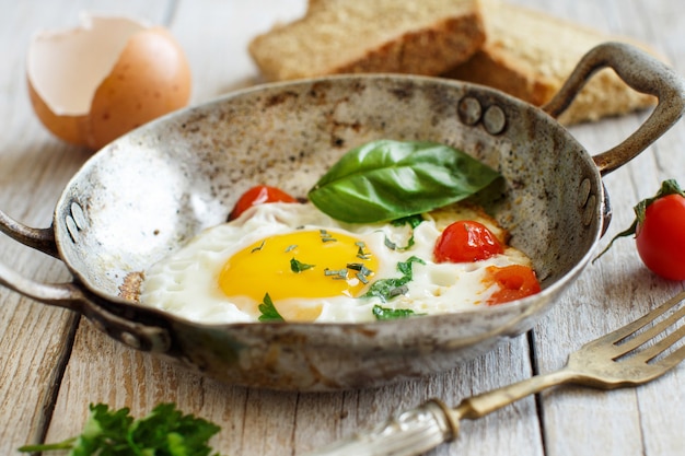 Œuf frit aux tomates, pain maison et herbes sur une vieille poêle à frire sur bois