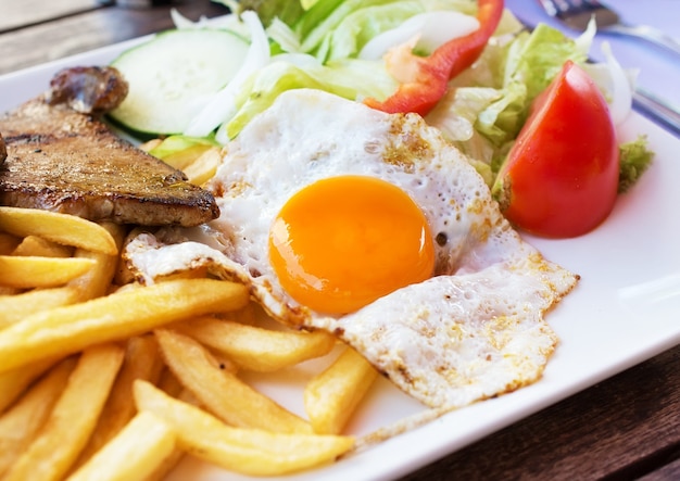 Œuf frit avec frites de pommes de terre, steak grillé et légumes.