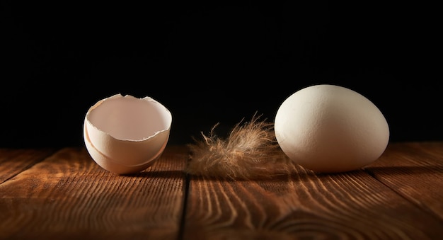 Œuf de poule et coquilles d'œufs sur une table en bois sur un fond sombre.