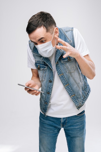 UFA, RUSSIE - 31 MARS 2020. Jeune homme en colère dans un masque respiratoire criant à quelqu'un dans son smartphone sur fond blanc.