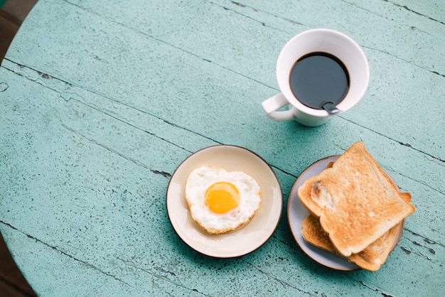 Œufs au plat, pain grillé, café, set de petit-déjeuner posé sur une table en bois bleue