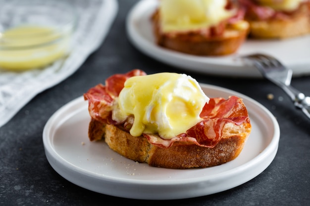 Œufs bénédictins - pain anglais grillé, jambon cru, œufs pochés à la sauce hollandaise et citron sur fond gris