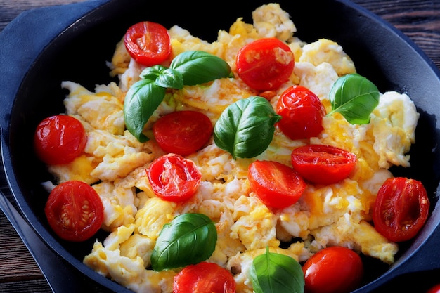 Œufs brouillés avec quartiers de tomates cerises et basilic frais dans une poêle en fonte