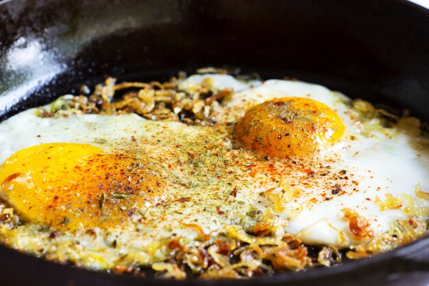 Œufs frits aux oignons et épices dans une poêle en fonte.