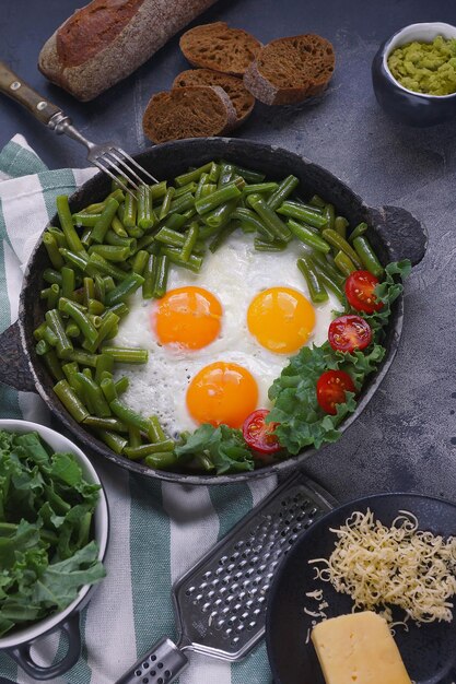 Œufs frits dans une vieille casserole avec tomates, pesto d'avocat, haricots verts, poivre et salade sur fond sombre