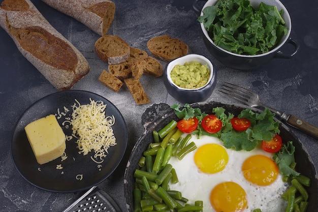 Œufs frits dans une vieille casserole avec tomates, pesto d'avocat, haricots verts, poivre et salade sur fond sombre