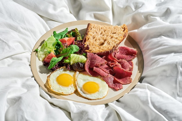 Œufs frits avec salade de légumes et rosbif dans une assiette sur une feuille blanche Lumière dure