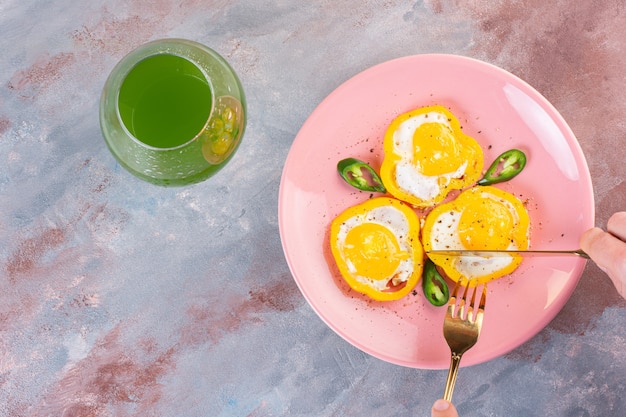 Œufs frits en tranches de poivrons jaunes et une tasse en verre de jus vert.